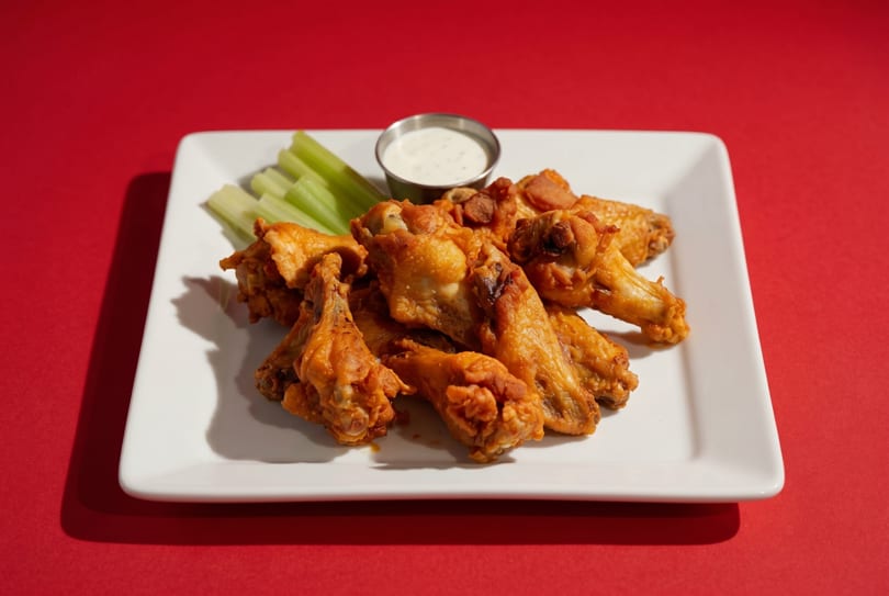 Plate of golden-brown chicken wings with celery sticks and a side of ranch dressing.