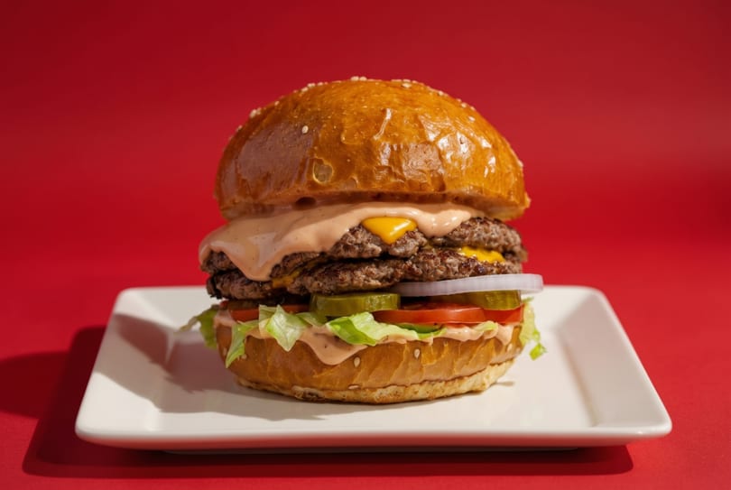 A double cheeseburger with special sauce, lettuce, tomato, pickles, and onions on a white plate.